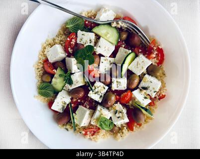 Couscous mit Feta und frischem Gemüse wie Tomaten, Gurken und Paprika, serviert in einer weißen Schüssel. Gesunde und vegetarische Lebensmittel. Stockfoto