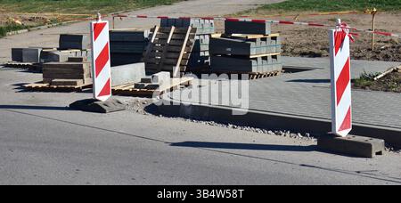 Viele Betonblöcke und Fliesen auf dem Straßenrekonstruktionsgelände. Straßenmarkierungen und Schilder, die Straßenumbauarbeiten zeigen. Paletten voll mit Stockfoto