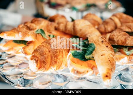 Frisch gebackene Croissants gefüllt mit aromatischem Räucherlachs und knusprigem Grün, angeordnet auf einer klaren Glasplatte, die die Textur unterstreicht und das Vis unterstreicht Stockfoto