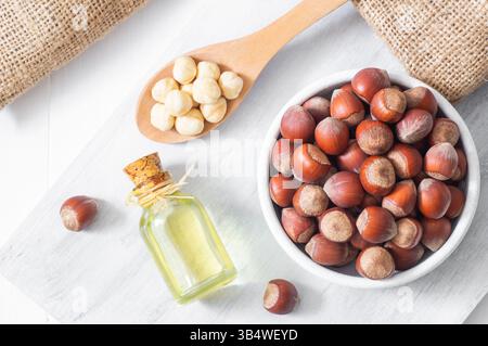 Haselnussöl, filbert und Kochöl in Glasflasche auf weißem Holztisch, Haufen oder Stapel Haselnüsse, gesundes Essen Stockfoto