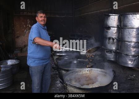 23. April 2022, Rafah, Gazastreifen, Palästina: Palästinenser kochen über Feuer. Suleiman Al-Aloul Madi verwendet seit 50 Jahren Feuer, um Speisen zu kochen, während er Mahlzeiten nach den Wünschen des Kunden zubereitet. Dies hilft ihm auch, die schwierigen Bedingungen im Gazastreifen zu überwinden. (Bild: © Samar Abu Elouf/ZUMA Press Wire Service) Stockfoto