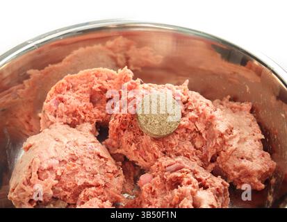 Hundefutter mit Medikamenten oder Vitaminpräparaten. Schüssel aus Edelstahl mit Rohfutter und großer Pille darauf. Medizin in nassem Tierfutter verstecken. Haustierzubehör Stockfoto