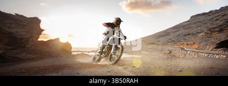 Fokussierte Biker fahren durch die Wüste Canyon mit Felsen und glühender Sonne im Hintergrund. Extreme Sportabenteuer. Zusammengesetztes Bild Stockfoto