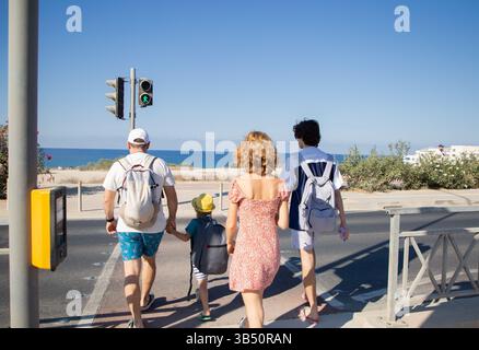 4 Touristen mit einem Kind überqueren die Fußgängerüberquerung mit einer grünen Ampel, die zum Uferdamm führt Stockfoto