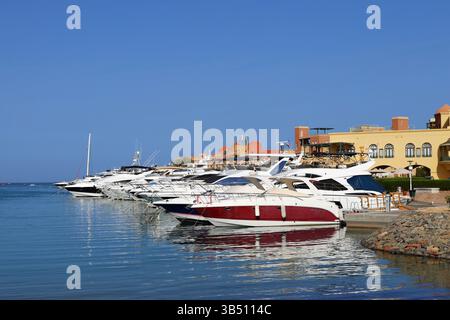 Luxusyachten legten an einem Jachthafen in El Gouna, Ägypten, an, mit klarem blauen Himmel und Gebäuden am Wasser, die sich im ruhigen Wasser des Roten Meeres spiegeln. Stockfoto