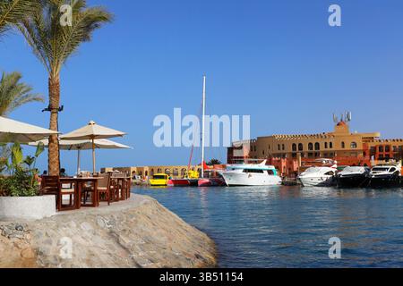 Luxusyachten legten an einem Jachthafen in El Gouna, Ägypten, an, mit klarem blauen Himmel und Gebäuden am Wasser, die sich im ruhigen Wasser des Roten Meeres spiegeln. Stockfoto