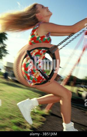 Junge Frau im Sommerkleid auf Schaukelsitz in Park Spielplatz. Stockfoto