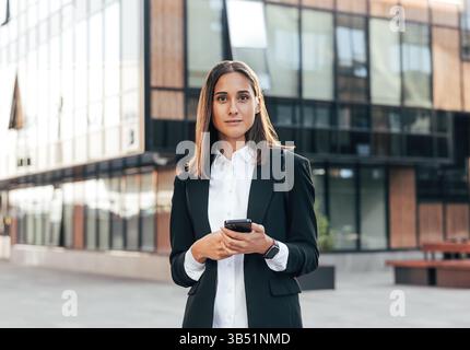 Porträt einer jungen Frau in formeller Kleidung, die draußen vor einem Bürogebäude steht Stockfoto