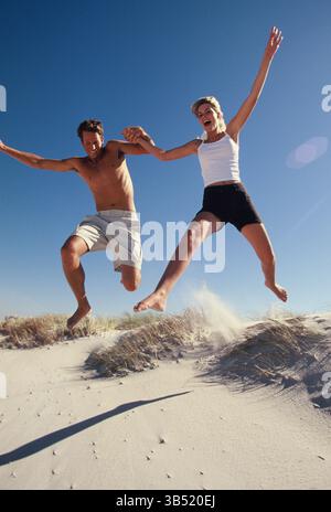Lifestyle. Glückliches junges Paar, das aus der Sanddüne am Strand springt. Stockfoto