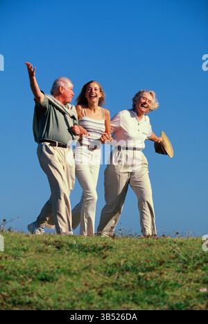 Seniorenpaar mit erwachsener Tochter, die auf einem grasbewachsenen Hügel draußen spaziert. Stockfoto