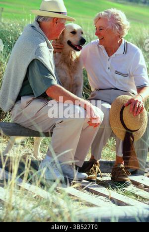 Senior Mann und Frau mit Haustier Labrador Hund sitzen draußen auf Parkbank. Stockfoto