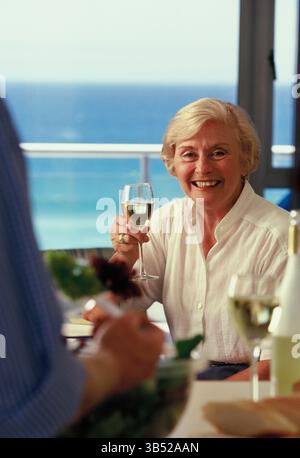 Seniorin trinkt Wein im Restaurant mit Meerblick. Stockfoto
