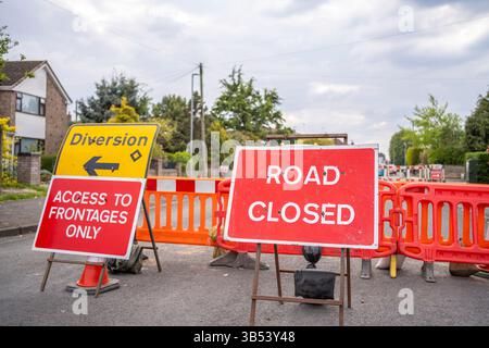 Straßensperrschild durch Barrieren auf einer Wohnstraße, die aufgrund von Gasarbeiten im Hintergrund geschlossen ist. Zugang zu Fronten und Umleitungsschildern sind ebenfalls vorhanden. Stockfoto