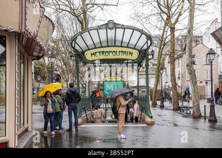 Menschen mit Sonnenschirmen vor dem Eingang der U-Bahn-Station „Abesses Art Nouveau“ an einem regnerischen Frühlingstag im Pariser Viertel Montmartre, Frankreich Stockfoto