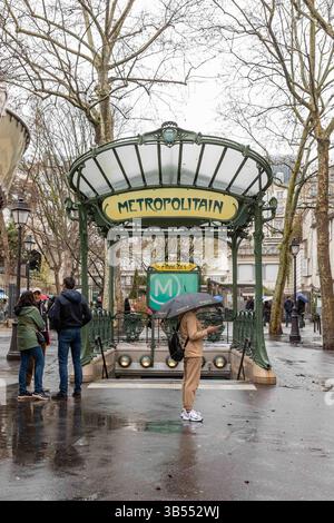 Frau mit Schirm steht vor der U-Bahn-Station Abbesses Jugendstileingang an einem regnerischen Frühlingstag im Montmartre-Viertel von Paris, Frankreich Stockfoto