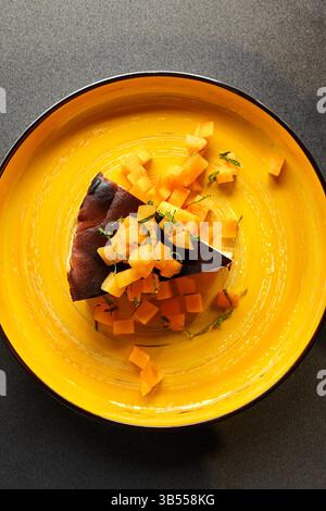 Stück von san sebastian verbranntem Käsekuchen, dekoriert mit Persimmon- und Minzblättern auf gelber Platte, Blick von oben Stockfoto