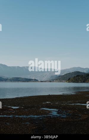 Friedlicher Blick auf den Skadar-See in Montenegro mit Bergsilhouetten im Hintergrund und flachem, strukturiertem Wasser im Vordergrund unter einem klaren blau Stockfoto
