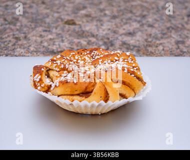 Ein frisch gebackenes Zimtbrötchen mit Sesamsamen darauf, in einen Papierbecher auf einer hellen Oberfläche gelegt. Stockfoto