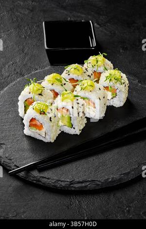 Frisch zubereitete Uamaki-Sushi-Brötchen werden auf einem schwarzen Schieferteller mit Lachs, Avocado und Frischkäse serviert, garniert mit Mikrogrün, SE Stockfoto