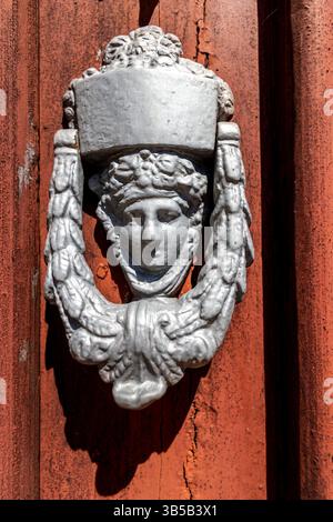 Nahansicht einer alten dekorierten Tür klopft in einer roten Holztür. Stockfoto