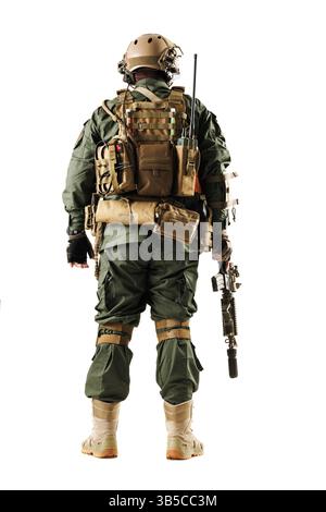 Ein stark ausgerüsteter taktischer Soldat in grüner Uniform, mit einer Schusswaffe, mit verschiedenen Ausrüstungen auf dem Rücken, gefangen gegen einen weißen Hintergras Stockfoto