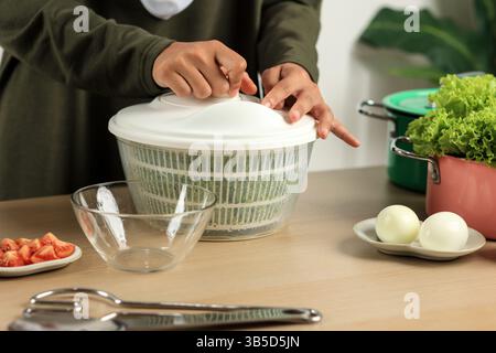 Frau lässt Salat aus dem Wasser in einer Salatschleuder abtropfen, Schritt für Schritt Salat in der Küche zubereiten Stockfoto