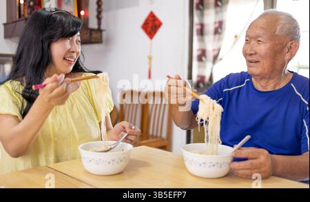Glücklicher älterer Vater und Tochter essen zu Hause Nudeln Stockfoto