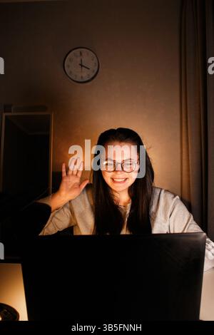 Lächelnde Frau grüßt geliebte Menschen mit Gesten, die während eines Videoanrufs einen Laptop benutzen. Schickt Liebe, jemand, der weit weg lebt. Online-Konferenz mit Freunden Stockfoto