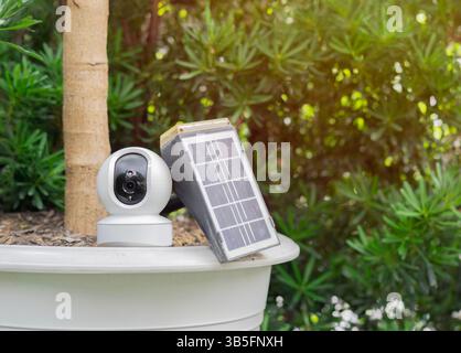 Ein kleines Solarmodul mit CCTV-Kamera auf dem großen weißen Topf im Garten. Kopierbereich. Stromerzeuger-Gadget-Konzept. Stockfoto