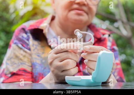 Aktive Seniorin mit Hörgerät über Naturhintergrund. Selektiver Fokus. Hörgerätekonzept. Stockfoto