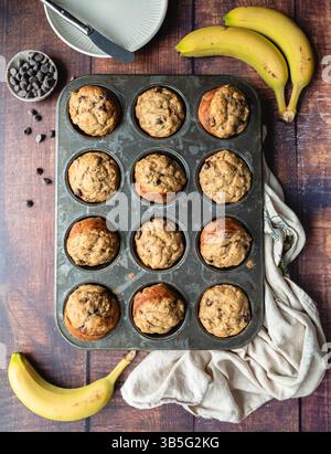 Blick von oben auf Bananenschokolade-Chips-Muffins in Blech auf Holztisch. Stockfoto