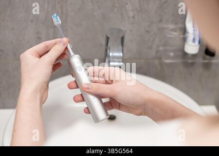 Halten Sie den Griff der elektrischen Zahnbürste und den abnehmbaren Bürstenkopf vorsichtig mit den Händen über ein Waschbecken, um die notwendigen Vorbereitungsschritte für e zu veranschaulichen Stockfoto