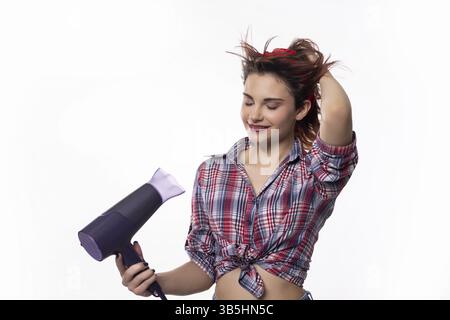Eine junge Frau trocknet ihr Haar mit einem Haartrockner und verleiht ihrem Stil eine lustige und trendige Atmosphäre Stockfoto