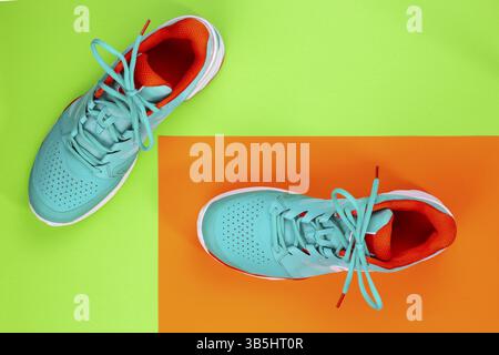 Rot, cyan, weiß, neue Tennisschuhe im Studio auf grünem, orangefarbenem Hintergrund. Direkt von oben Stockfoto