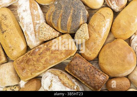 Viele Brotsorten und Brötchen, die zufällig nebeneinander auf einer hölzernen Arbeitsplatte platziert werden, als Dekoration einer traditionellen Bäckerei mit einer Mehrgenerationenorganisation Stockfoto