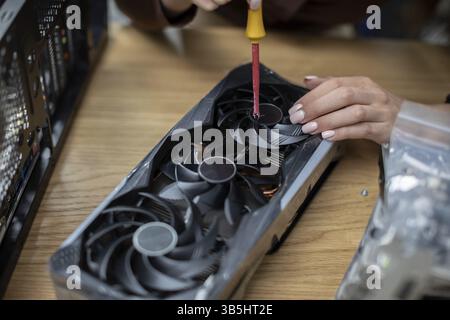 Nahaufnahme der Hände einer Frau. Die Frau hält einen Schraubenzieher in der Hand, mit dem sie ein Computerteil repariert. Der Computerteil liegt auf einer braunen Stockfoto