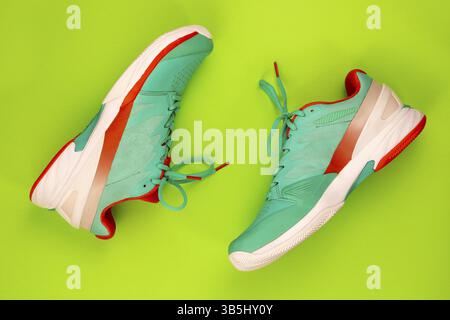 Rote, zyanblaue, weiße Tennisschuhe im Studio, auf grünem Hintergrund. Direkt von oben Stockfoto