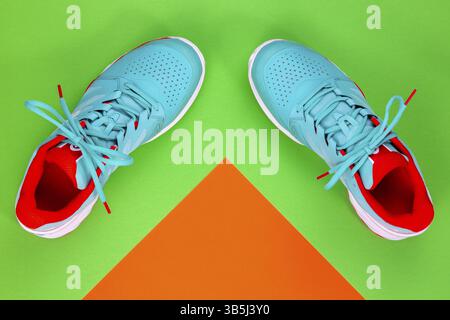 Rot, cyan, weiß, neue Tennisschuhe im Studio auf grünem und orangefarbenem Hintergrund. Direkt von oben Stockfoto