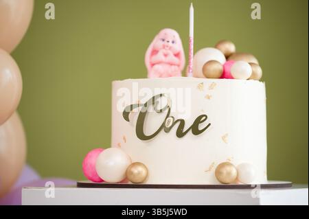 Ein köstlich aussehender weißer Kuchen, dekoriert für einen ersten Geburtstag. Rosa- und Goldakzente schmücken den Kuchen und schaffen eine festliche und charmante Atmosphäre. Stockfoto