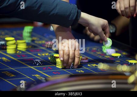 Roulette-Tisch mit menschlichen Händen, die Chips im Casino ablegen. Roulette-Rad im Vordergrund. Glücksspiel. Nicht erkennbare Personen Stockfoto