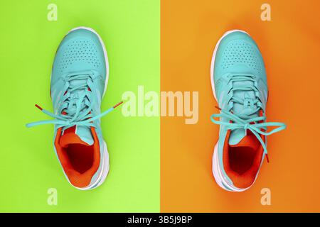Rot, cyan, weiß, neue Tennisschuhe im Studio auf grünem, orangefarbenem Hintergrund. Direkt von oben Stockfoto