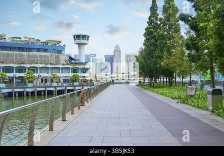 Modernes Stadtbild von singapur mit einer gepflasterten Promenade, die von Bäumen gesäumt ist, bietet malerische Ausblicke auf die Skyline der Stadt und das Wasser Stockfoto