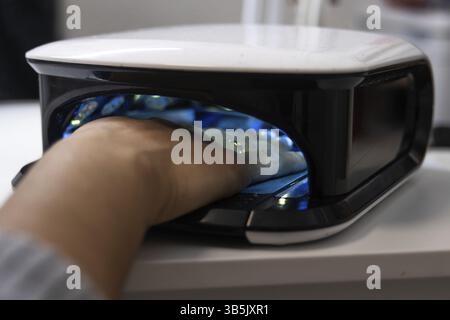 Nahaufnahme der Hand eines Kunden in einem UV-Nageltrockner, die während einer Maniküre den lack aushärtet Stockfoto