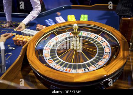 Roulette-Tisch im Kasino. Ball in der rotierenden Spielmaschine. Roulette-Rad aus Holz. Casino Croupier, der Roulette-Chips verkauft Stockfoto