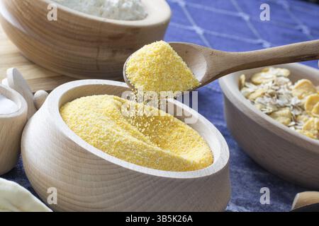Weibliche Hand aufheben Mais Mehl mit einem Holzlöffel aus Holzschale auf das Homeboard Stockfoto