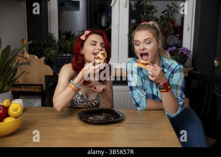 Zwei fröhliche Freunde essen gemeinsam köstliche Pizza an einem gemütlichen Holztisch in einer warmen Küchenatmosphäre Stockfoto