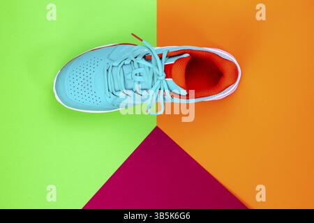 Rot, cyan, weiß, neuer Tennisschuh im Studio auf grünem, orangefarbenem, violettem Hintergrund. Direkt von oben Stockfoto