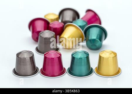 Farbenfrohe Kaffeekapseln auf weißem Hintergrund mit leuchtenden Rosa-, Gold-, Petrol- und Silbertönen. Arrangement schafft lebendige und lebhafte Atmosphäre Stockfoto