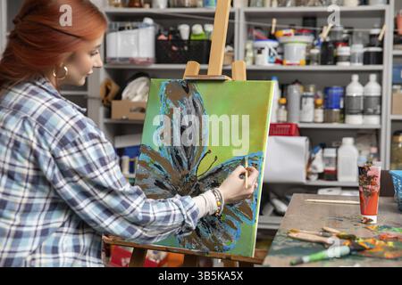 Ein talentierter junger Künstler malt eine lebendige Blume auf einer Leinwand in einem farbenfrohen Atelier voller Kunstgegenstände Stockfoto