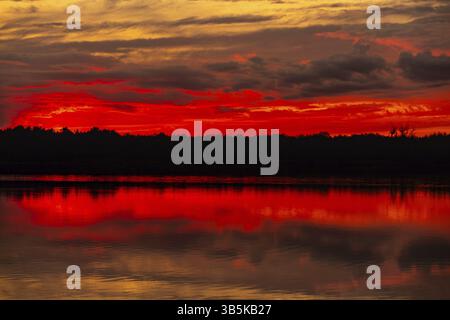 Ein atemberaubender Sonnenuntergang strahlt lebendige Farben über das ruhige Wasser des ruhigen Sees und schafft eine malerische Aussicht Stockfoto